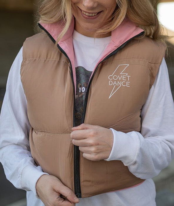 Person wearing a tan vest with 'Covet Dance' logo, smiling outdoors.