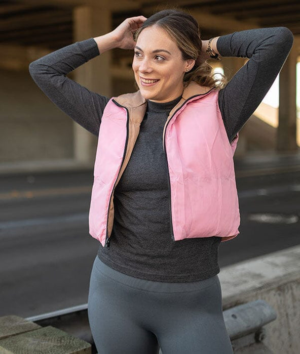 Woman wearing a pink puffer vest over a dark long-sleeve shirt and gray leggings, standing outdoors.