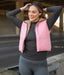 Woman wearing a pink puffer vest over a dark long-sleeve shirt and gray leggings, standing outdoors.