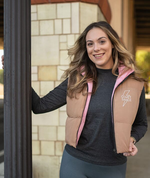 Woman wearing a beige and pink vest with a logo, standing outdoors.