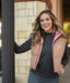 Woman wearing a beige and pink vest with a logo, standing outdoors.