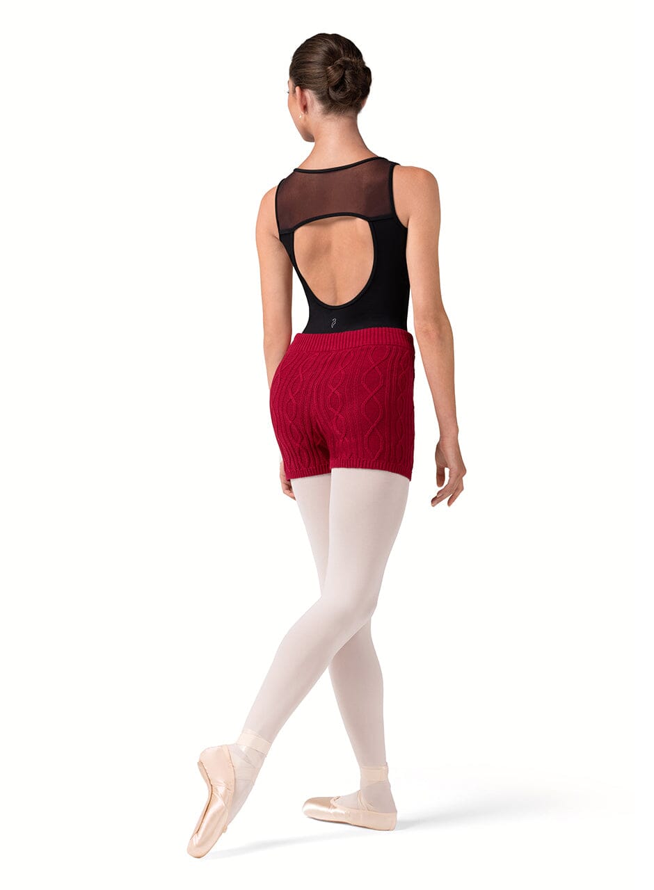 Ballerina in a black top and red shorts with white tights on a white background