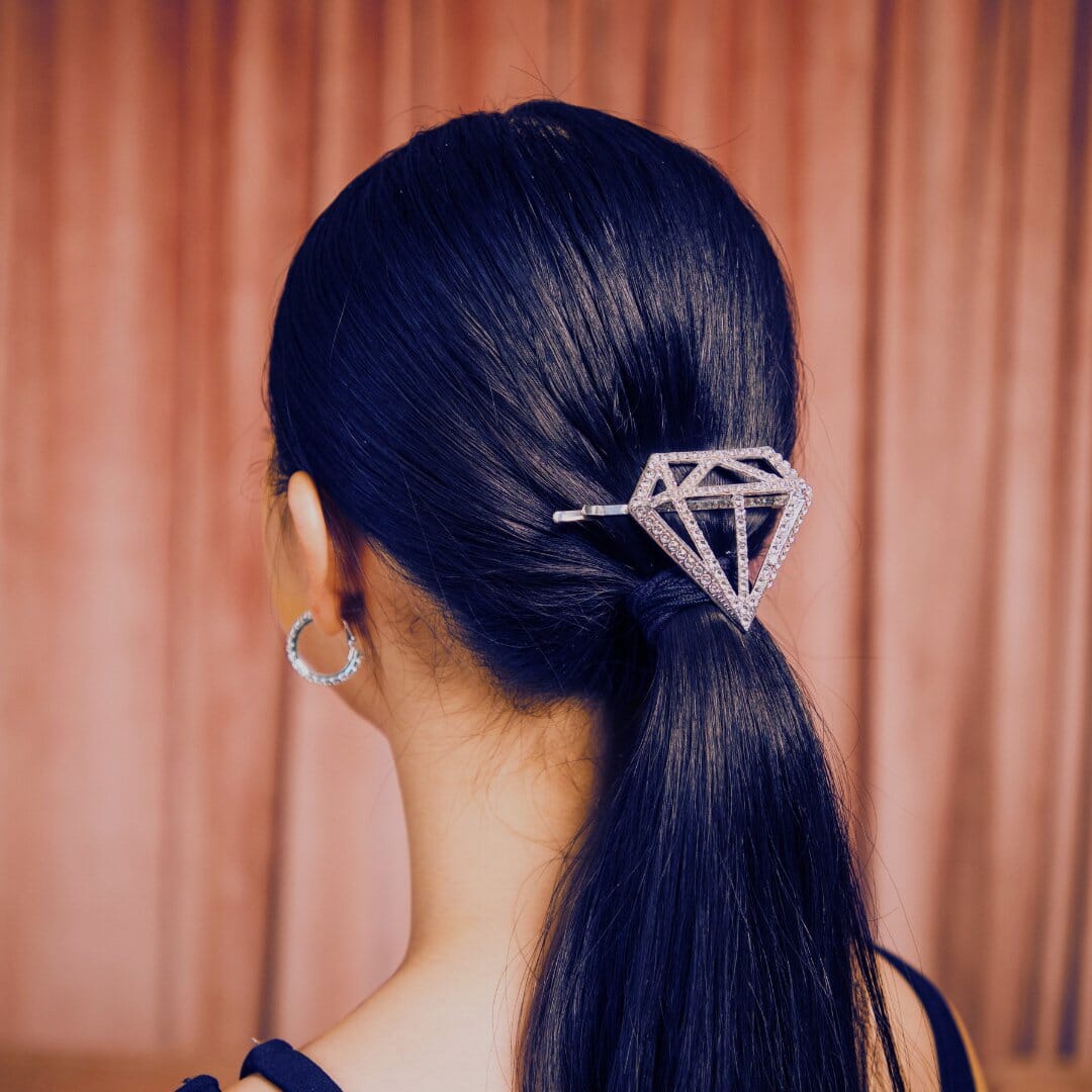 Person with a diamond-shaped hair clip in their dark hair against a pink curtain background