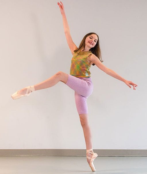 Dancer in a colorful top and purple leggings posing against a plain background