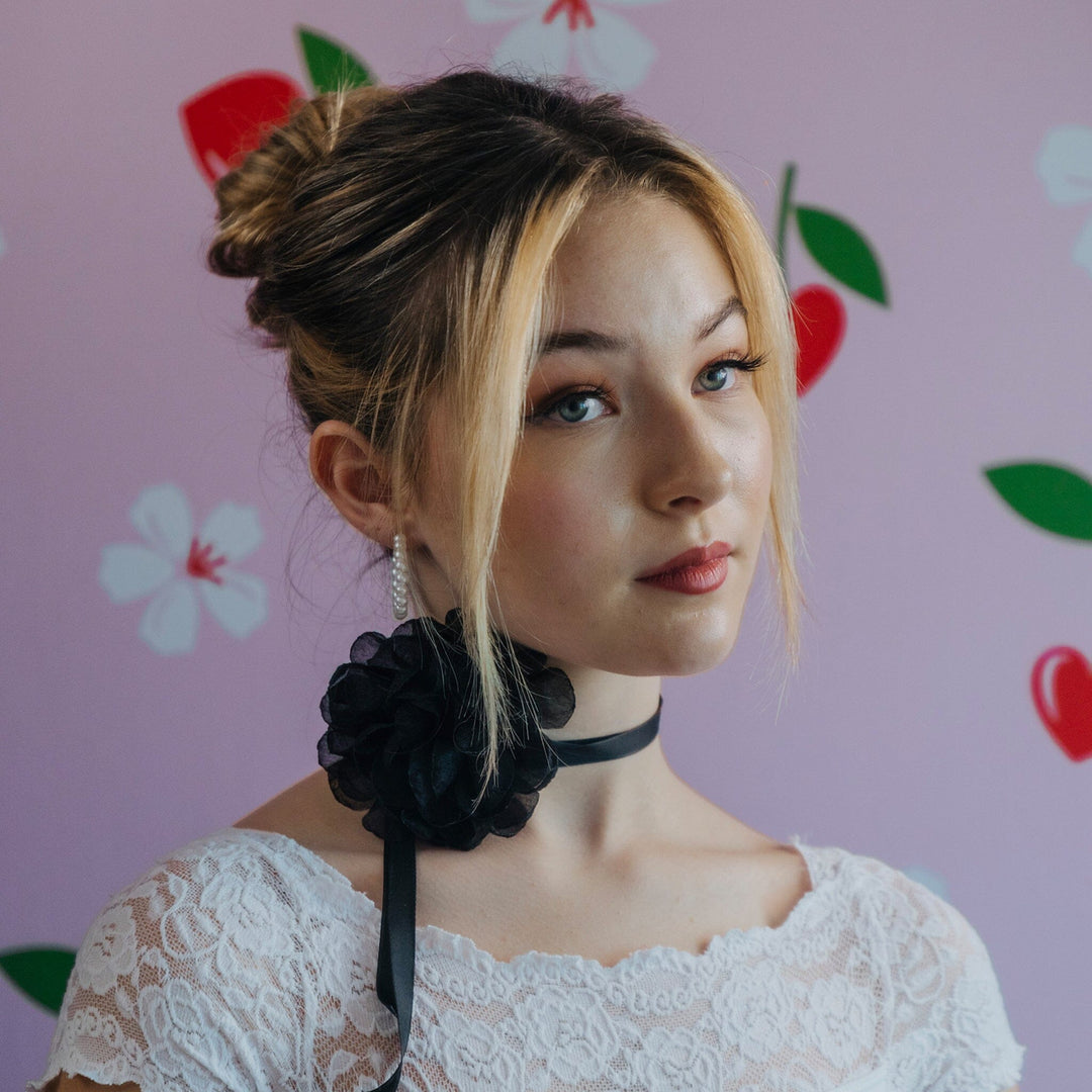 Woman wearing a black floral choker against a pink background with floral patterns