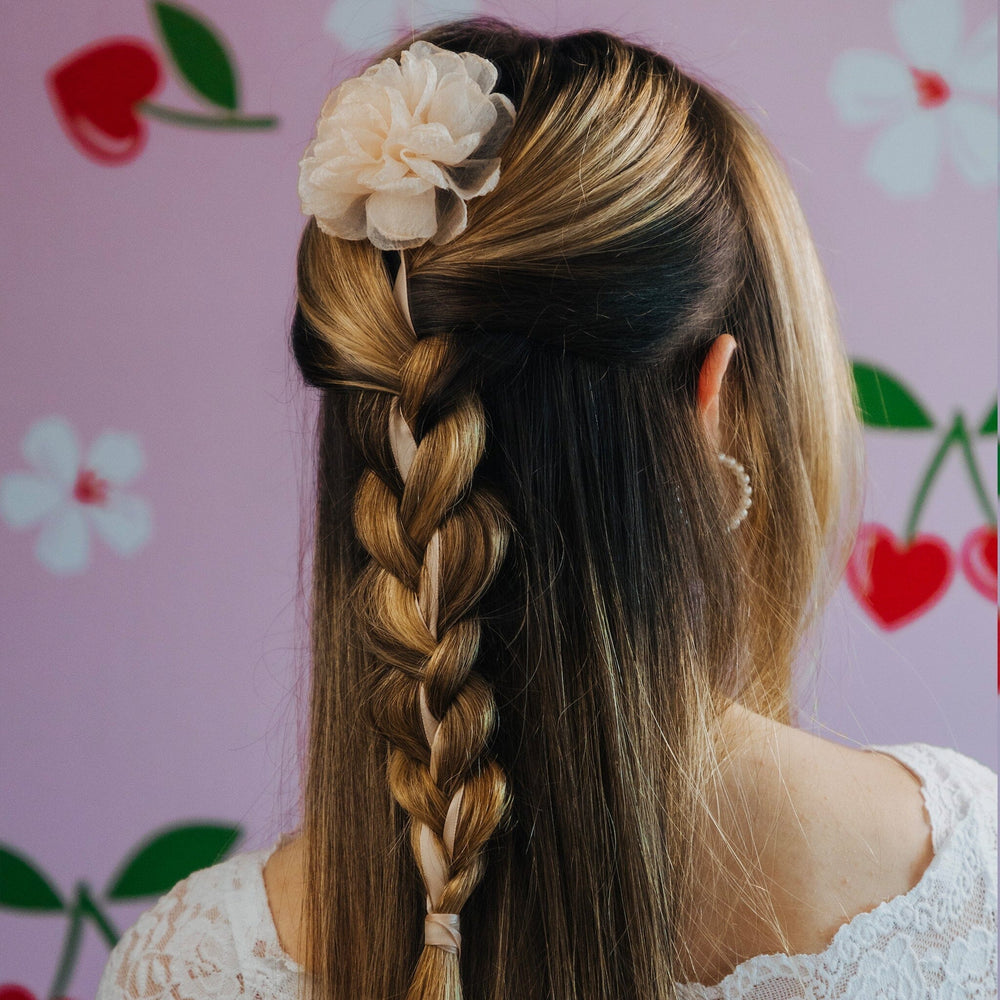 Woman with braided hair and floral accessory against a pink background with floral patterns