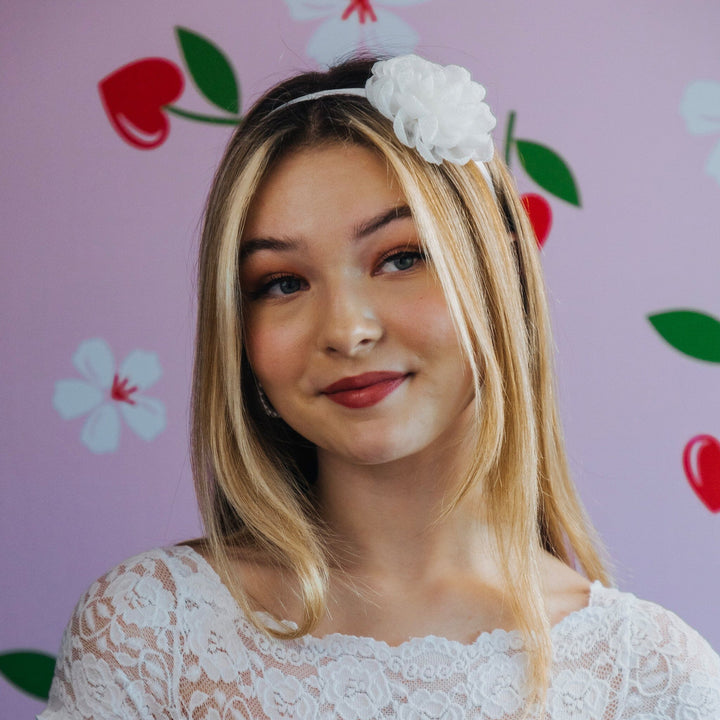 Woman wearing a white lace top and floral headband against a pink background with floral patterns.