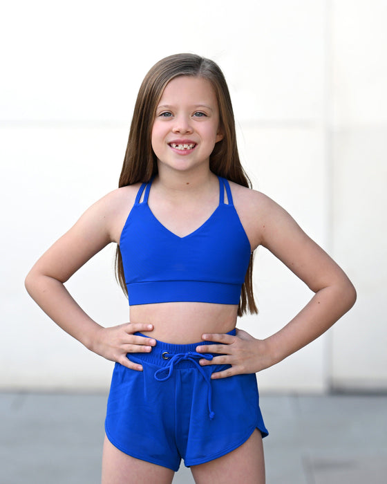 Young girl wearing a blue sports bra and shorts set on a plain background