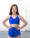 Young girl wearing a blue sports bra and shorts set on a plain background