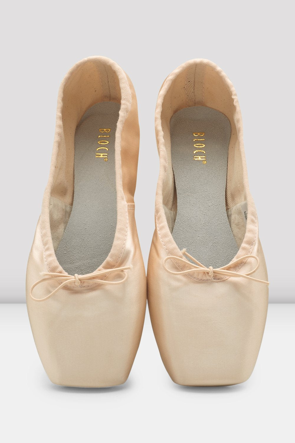 Pair of beige ballet shoes with a bow on a light gray background