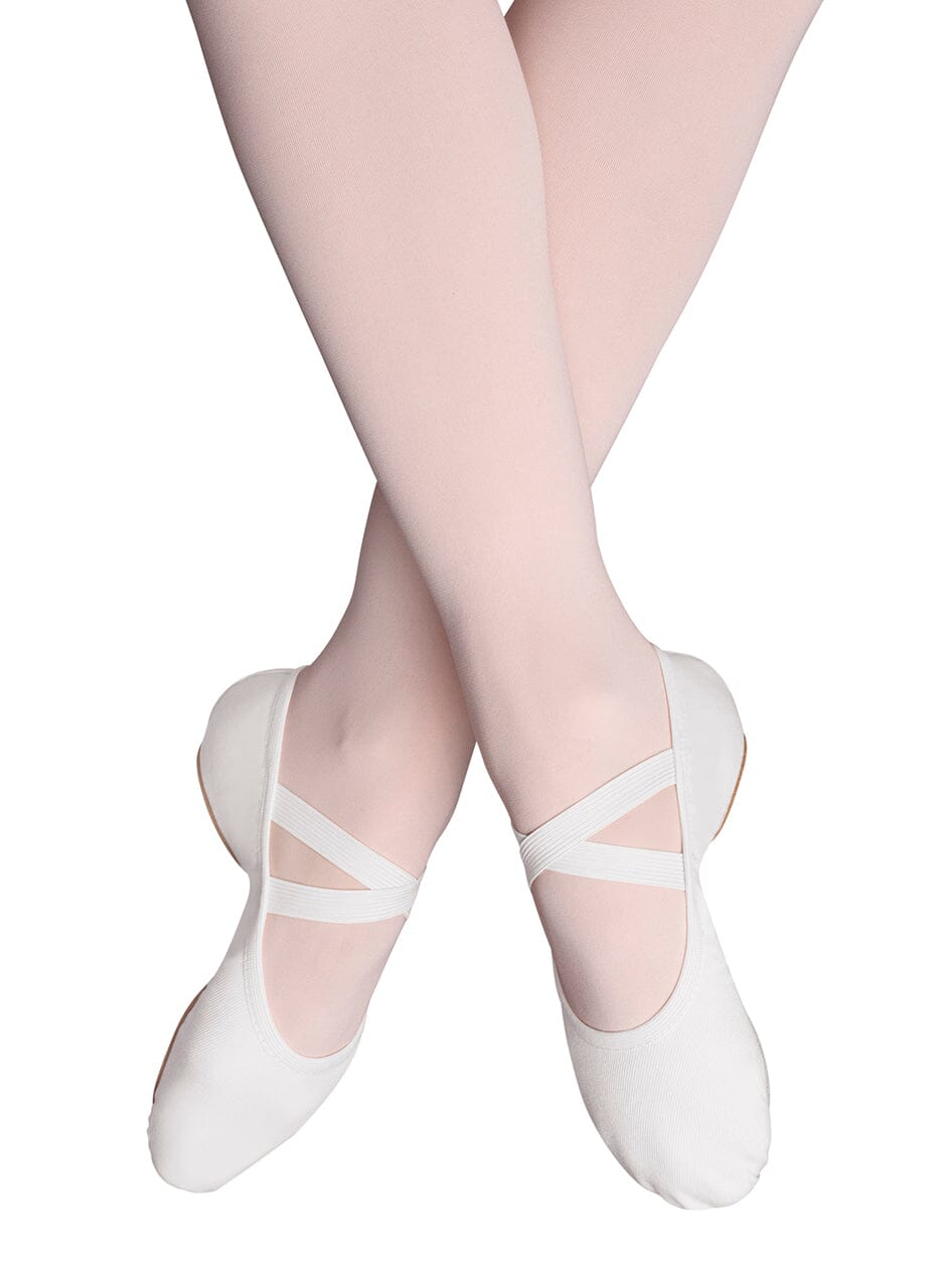 White ballet shoes worn with sheer pink tights on a white background