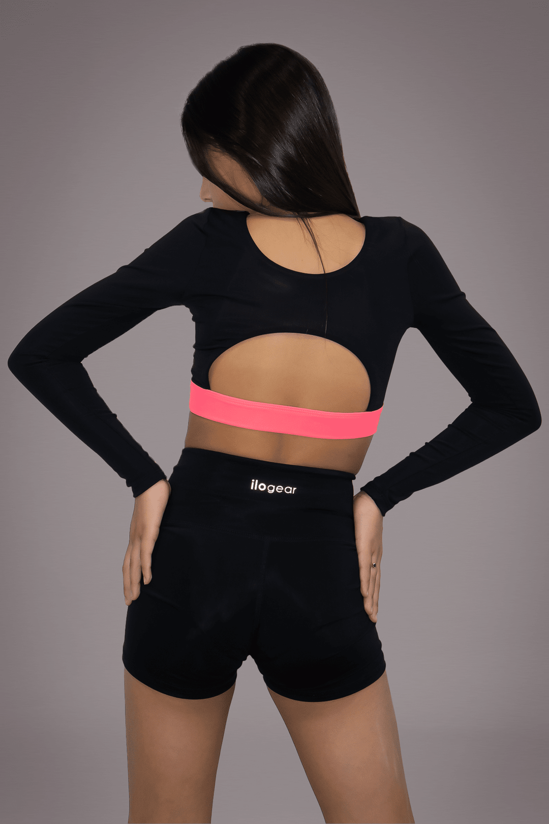 Person wearing a black long-sleeve crop top and black shorts with pink waistband on a gray background