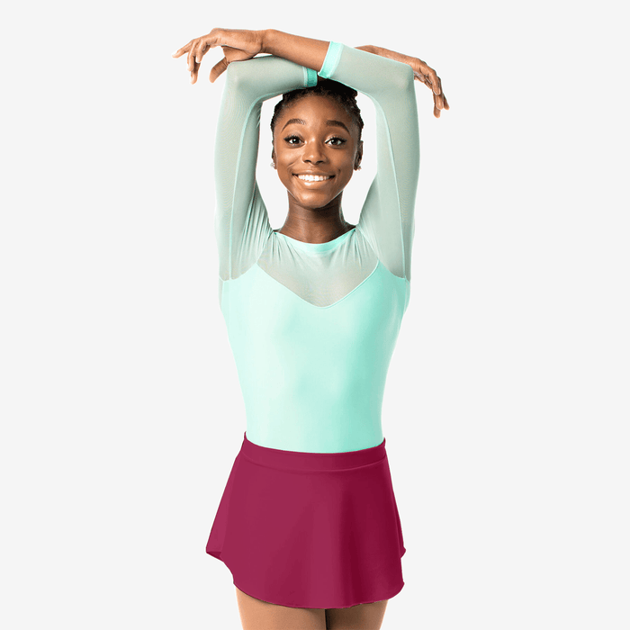 Young girl in a light green top and pink skirt posing against a white background