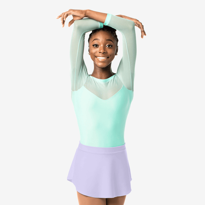 Young girl in a light green top and lavender skirt posing against a white background