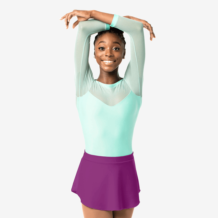 Young girl in a light green top and purple skirt posing against a white background