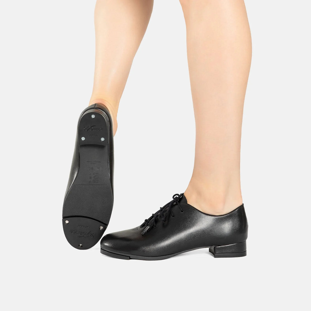 Black tap shoes worn by a person on a white background