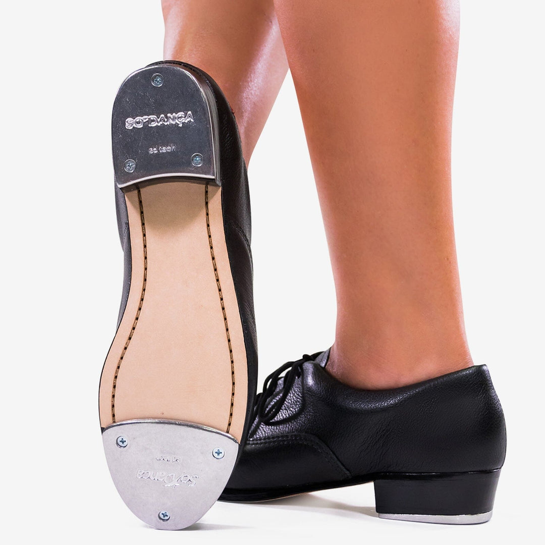 Black tap dance shoe with brand name on sole, worn by a person.