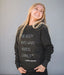 Woman wearing a black sweatshirt with a quote on it against a gray background