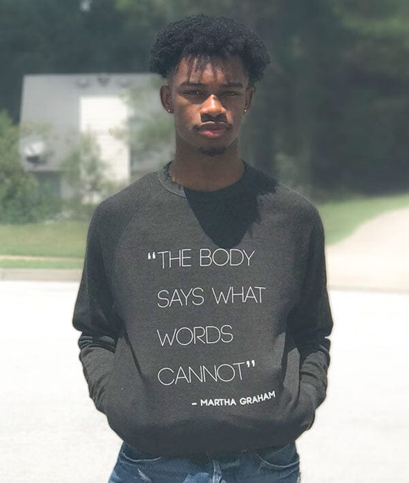 Person wearing a dark gray sweatshirt with a quote, standing outdoors.