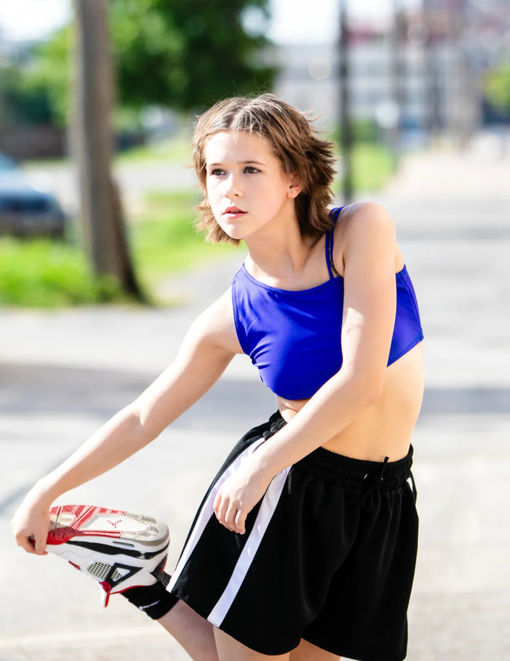 Woman in athletic wear holding a tennis racket on a street.
