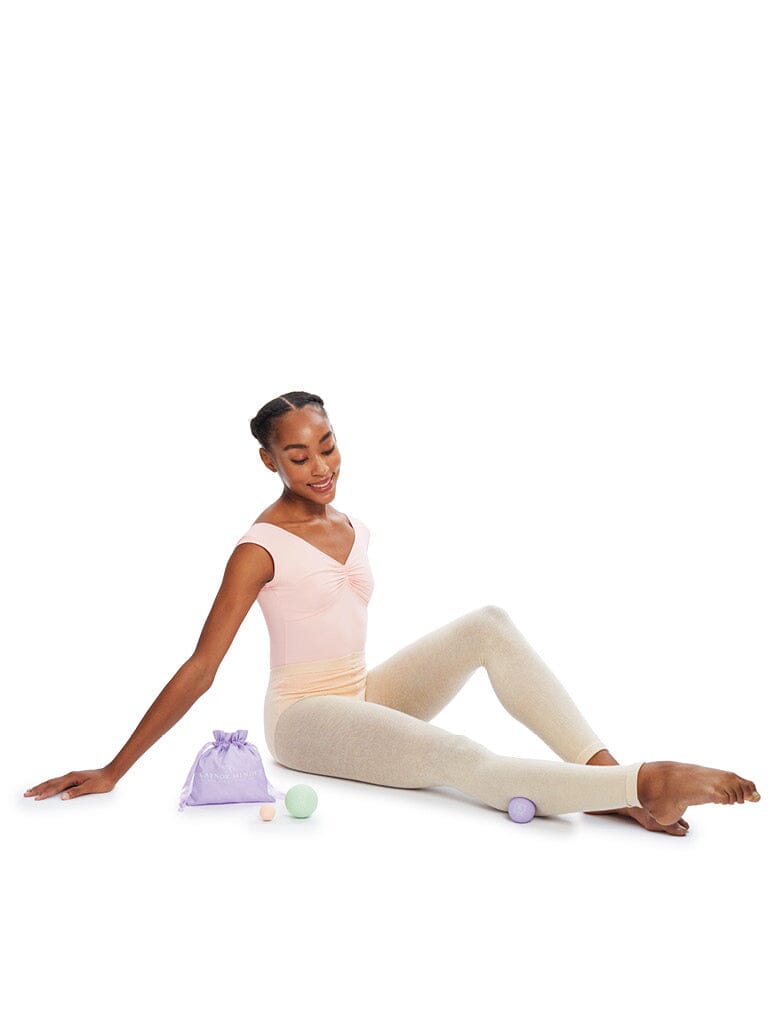 Ballerina sitting on a white background with ballet shoes and a bag.