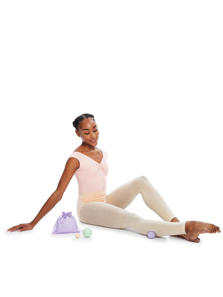 Ballerina sitting on a white background with ballet shoes and a bag.