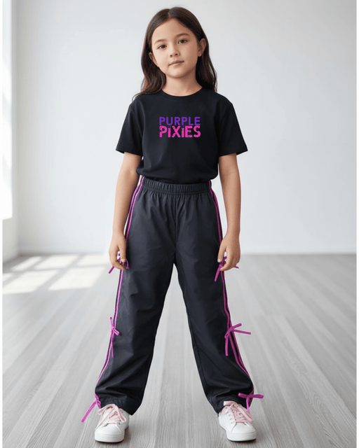 Young girl wearing a black t-shirt with 'Purple Pixies' text and black pants with pink accents on a light wooden floor.