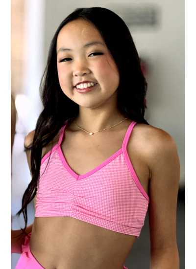 Young girl wearing a pink checkered sports bra and shorts.