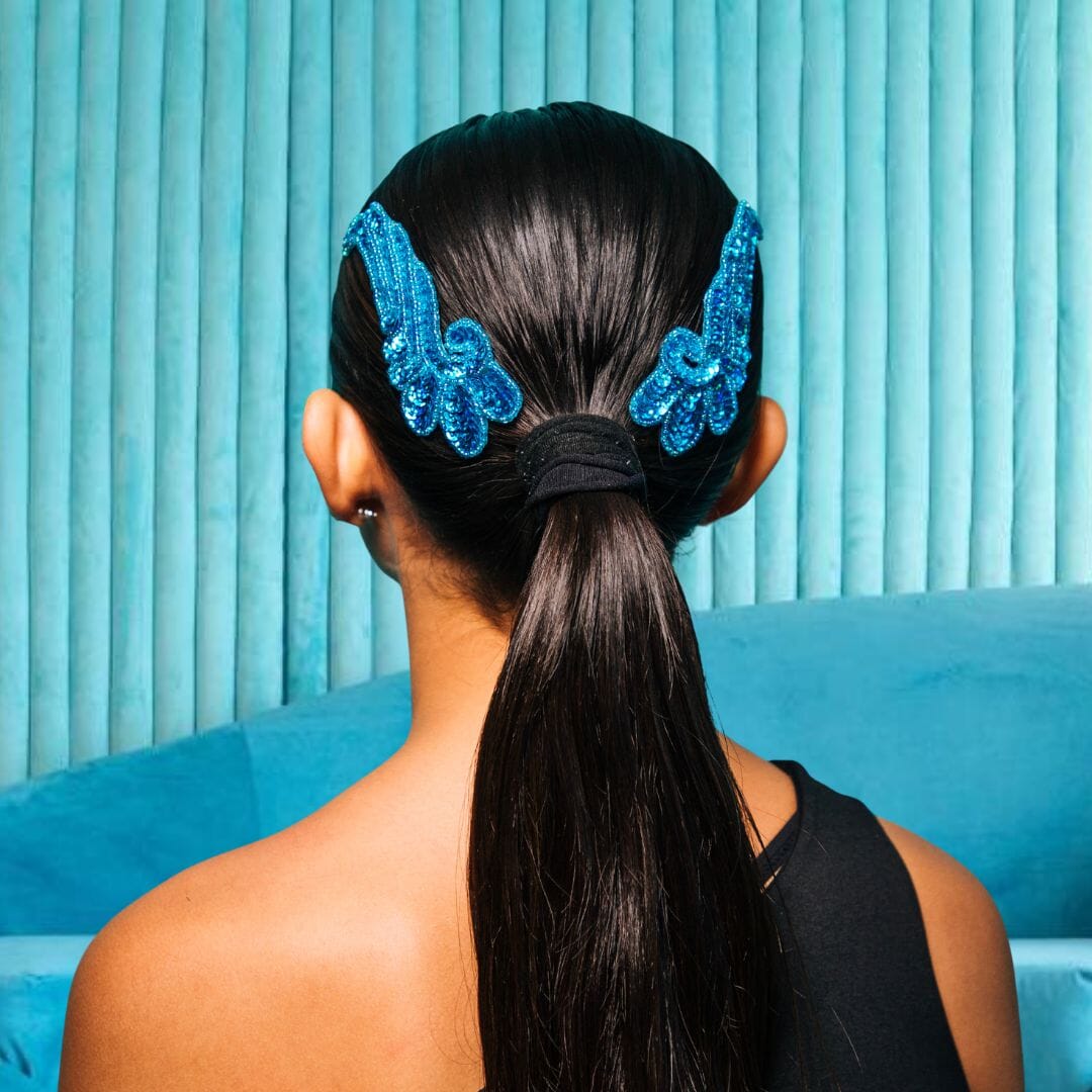 Person with a high ponytail wearing blue decorative hair accessories against a blue curtain background