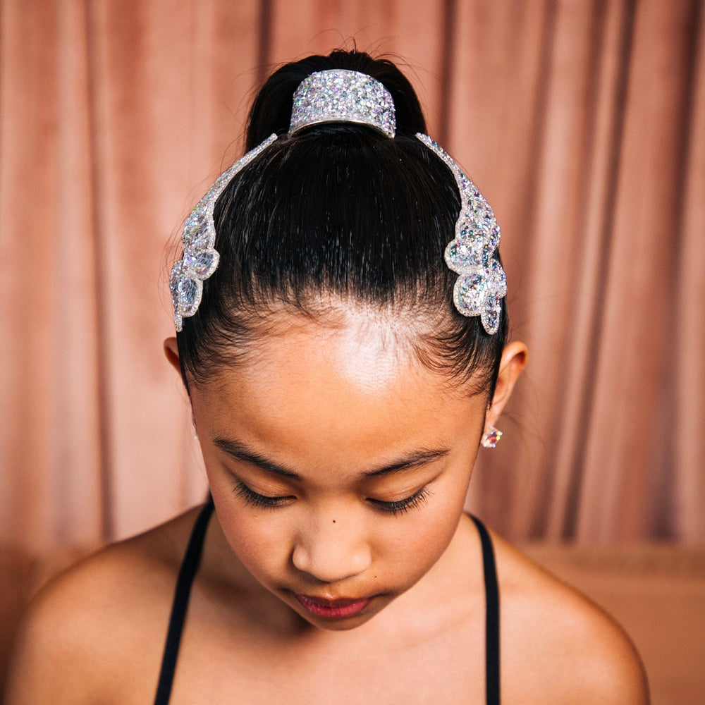 Young girl wearing a sparkling headband against a pink curtain background