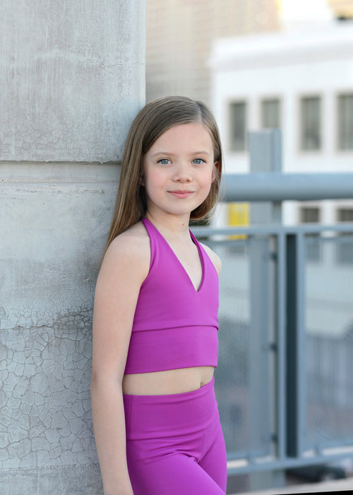 Young girl in a purple outfit standing against a textured wall with a blurred background