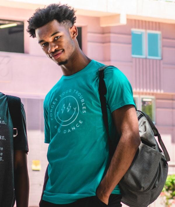 Man wearing a teal t-shirt with text, standing outdoors with a blurred background