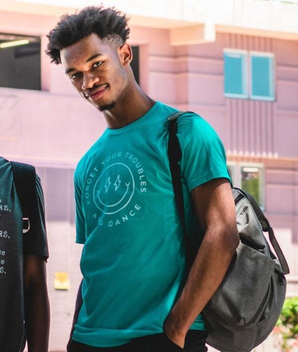 Man wearing a teal t-shirt with text, standing outdoors with a blurred background