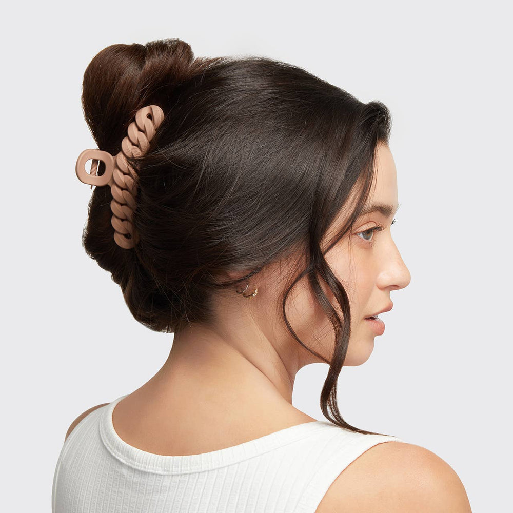 Woman with hair styled in a bun using a hair tie against a plain background