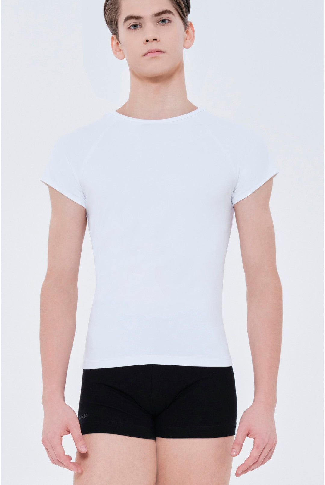 A male model wearing a fitted white short-sleeve crewneck t-shirt and black boxer briefs, photographed against a clean light gray studio background.