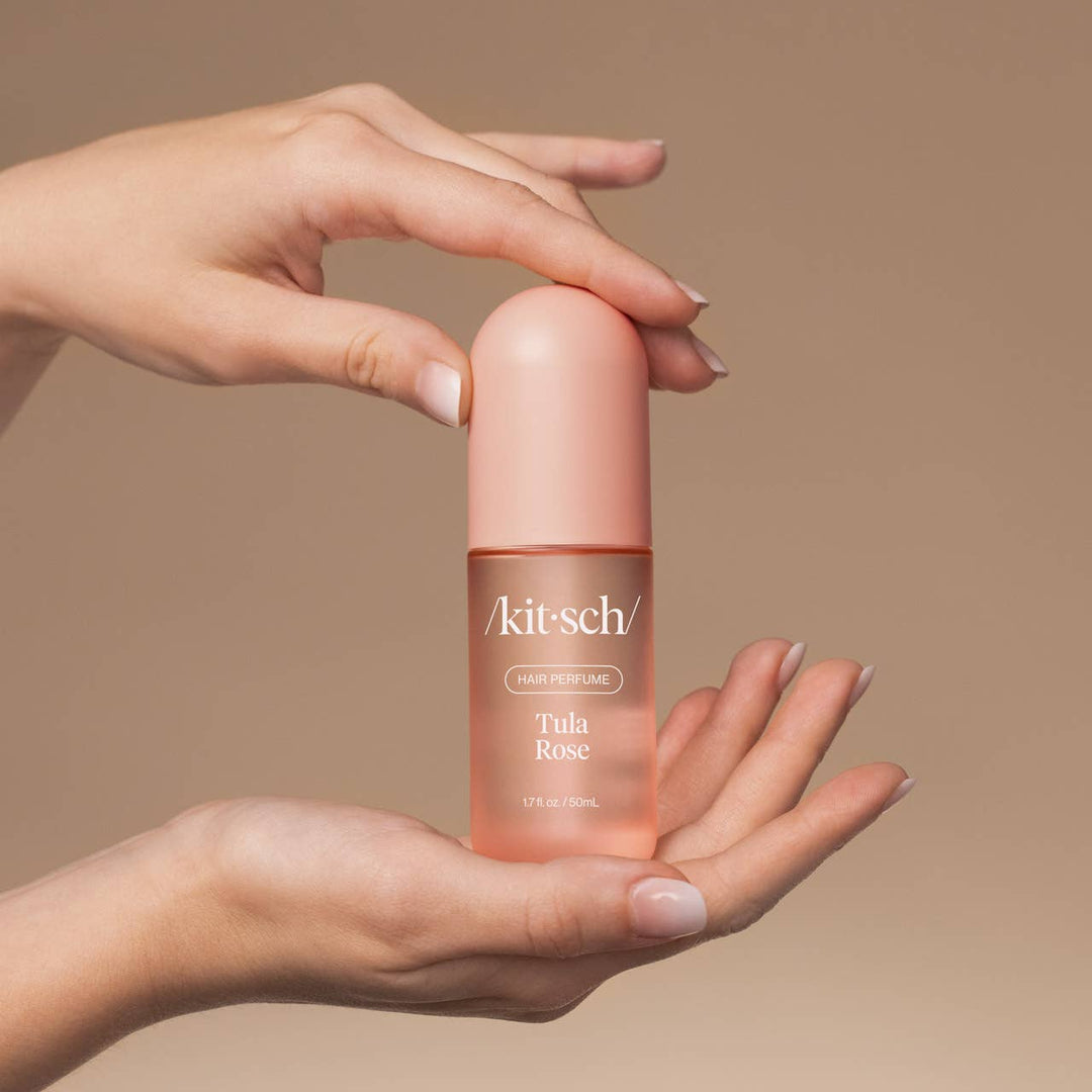 Hand holding a pink bottle of Kitsch Tula Rose hair perfume against a beige background