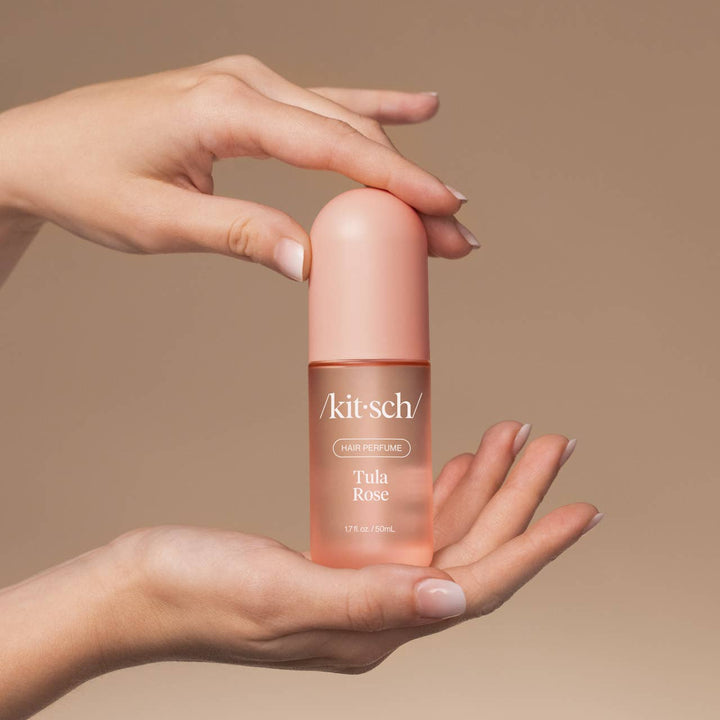 Hand holding a pink bottle of Kitsch Tula Rose hair perfume against a beige background