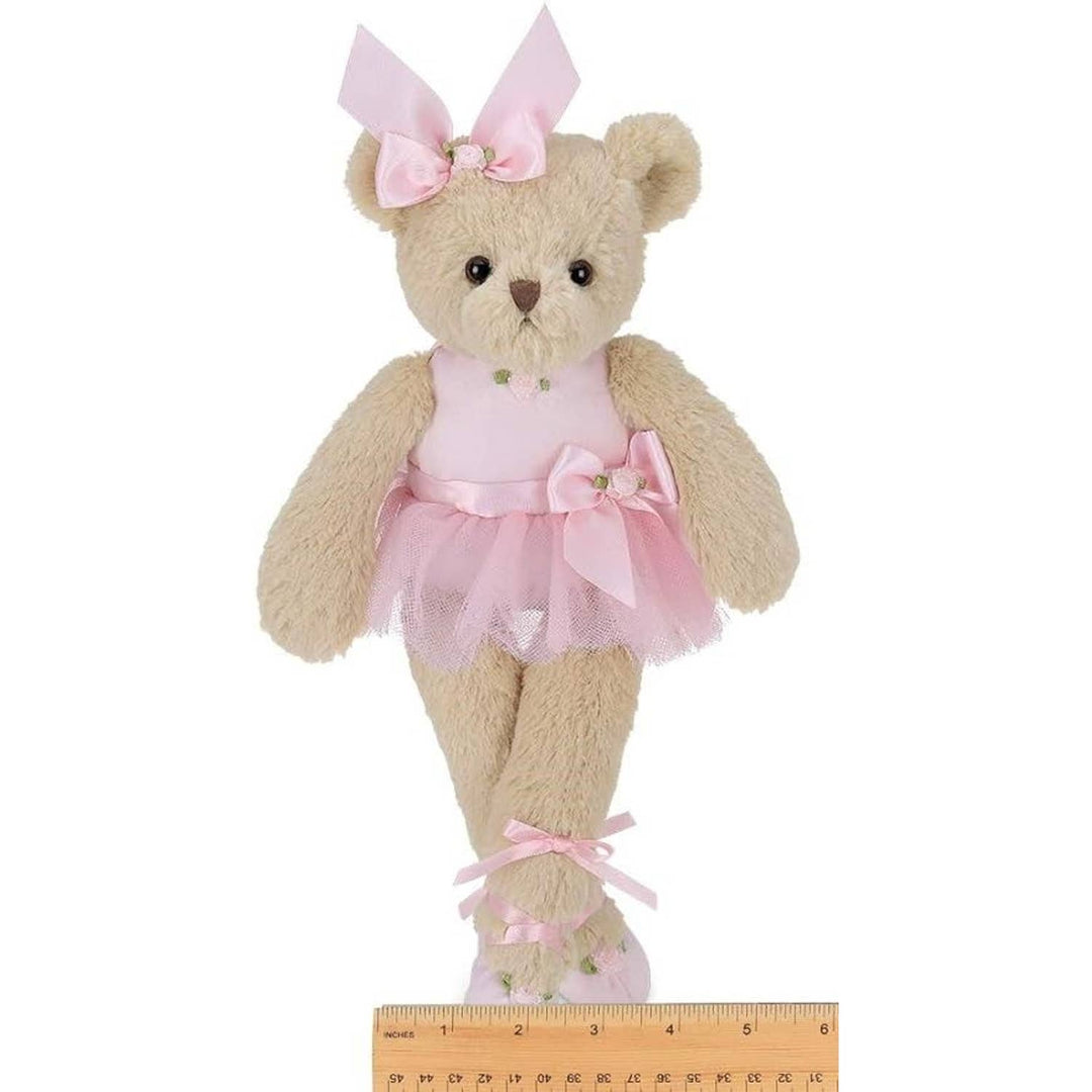 Teddy bear in a pink dress with a bow, standing next to a ruler for size reference.