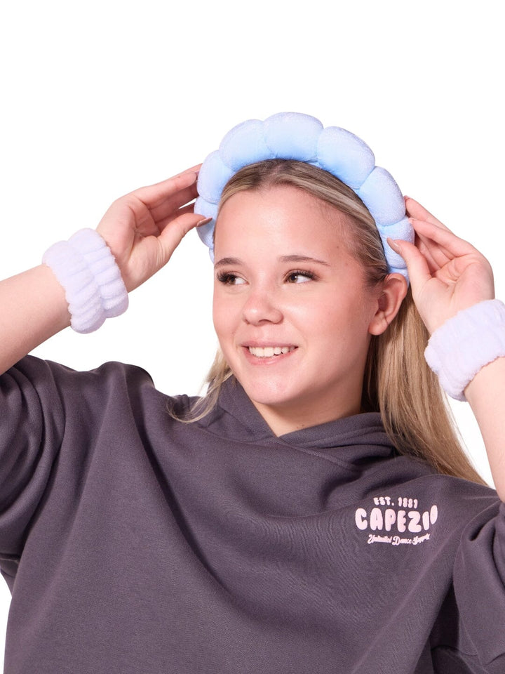 Person wearing a gray hoodie with a logo, holding a blue headband on a white background