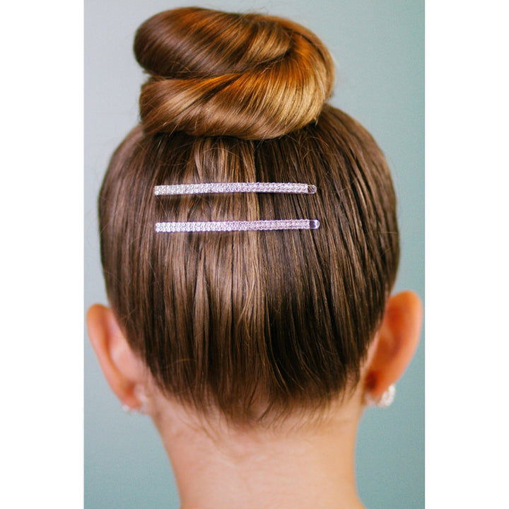 Person with a bun hairstyle featuring two decorative hairpins on a plain background