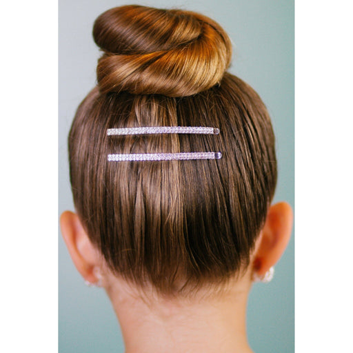 Person with a bun hairstyle featuring two decorative hairpins on a plain background