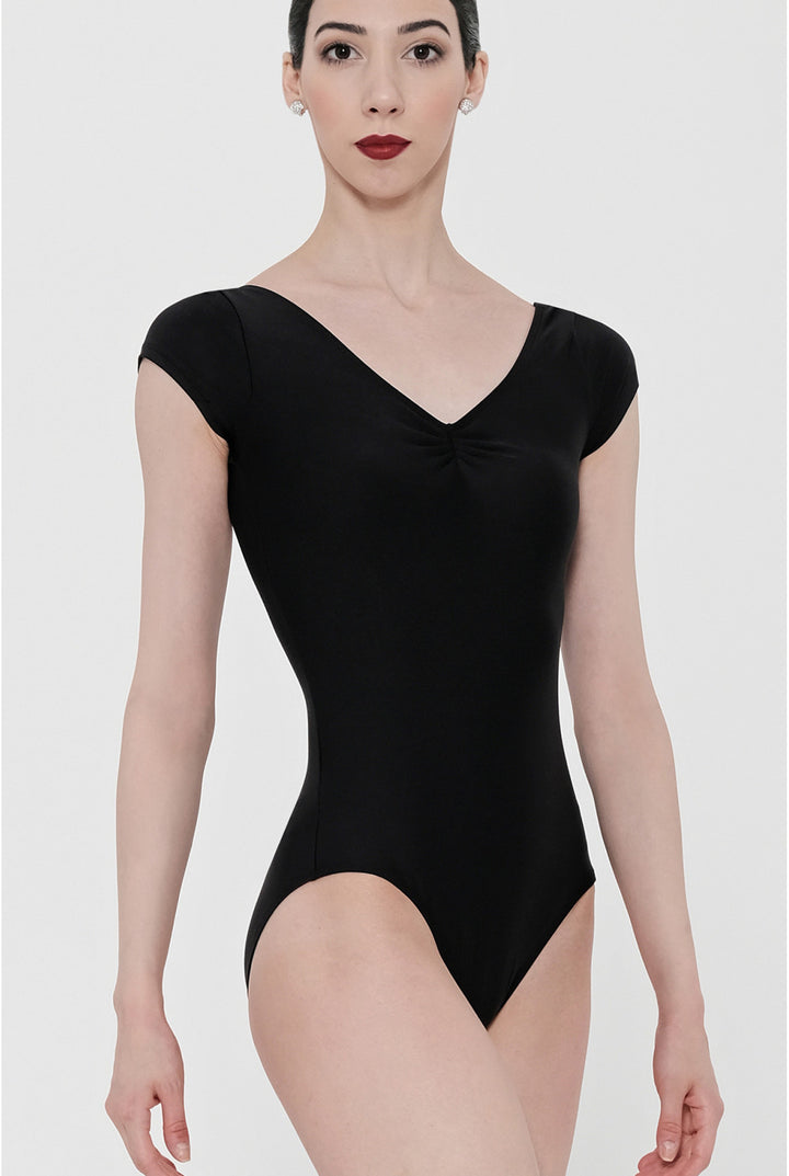 A woman modeling a black short-sleeve bodysuit with a V-neckline and a small gathered detail at the center chest, photographed against a light gray studio background.