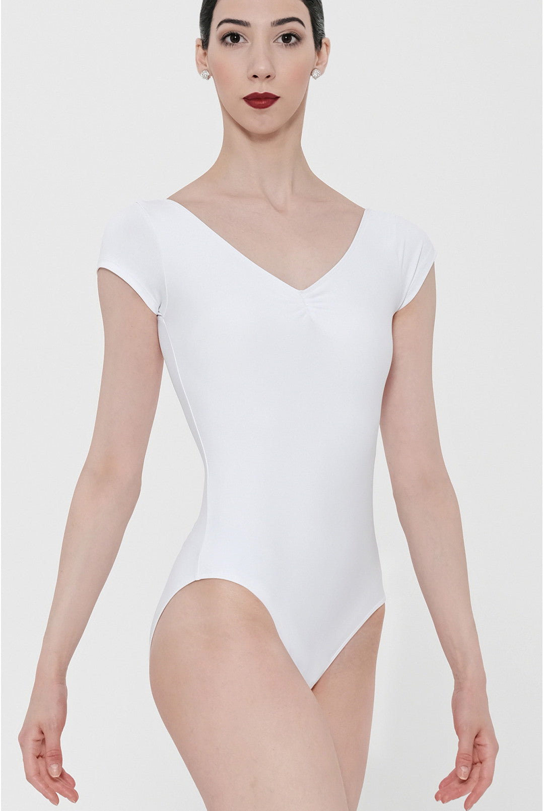A woman modeling a white short-sleeve V-neck leotard against a plain light gray studio background.