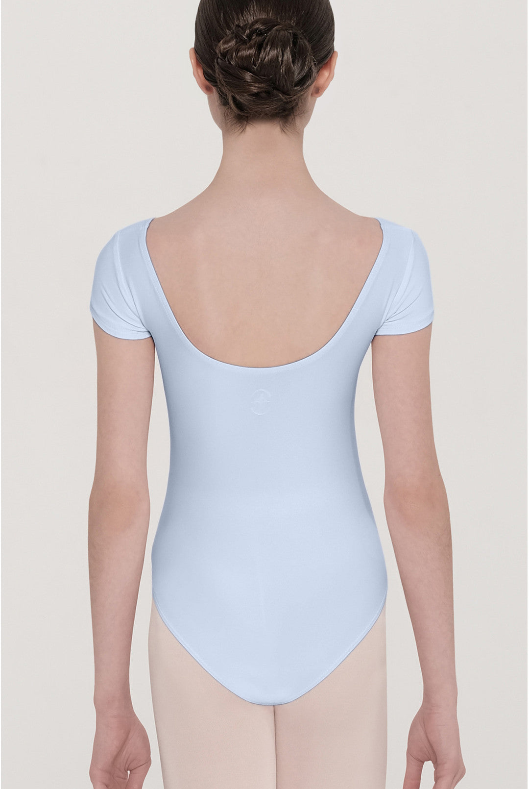 A dancer viewed from the back wearing a light blue short-sleeve leotard and nude tights against a light gray studio background.