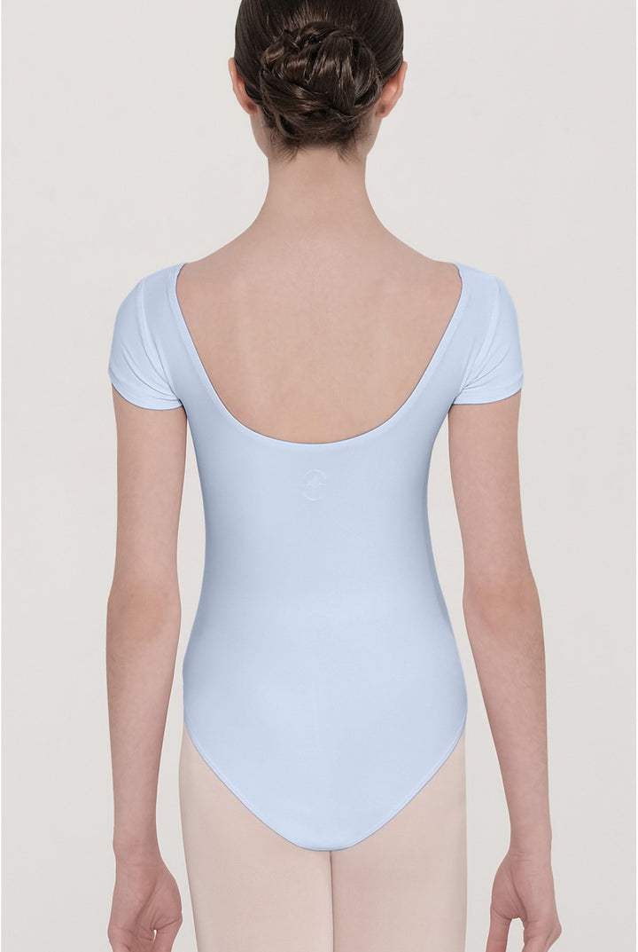 A dancer viewed from the back wearing a light blue short-sleeve leotard and nude tights against a light gray studio background.