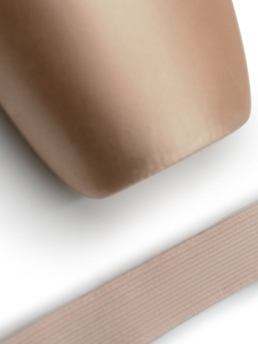 A close-up of a smooth, rounded beige object with a ribbed dusty pink strap or band running diagonally across the lower portion, set against a clean white background.