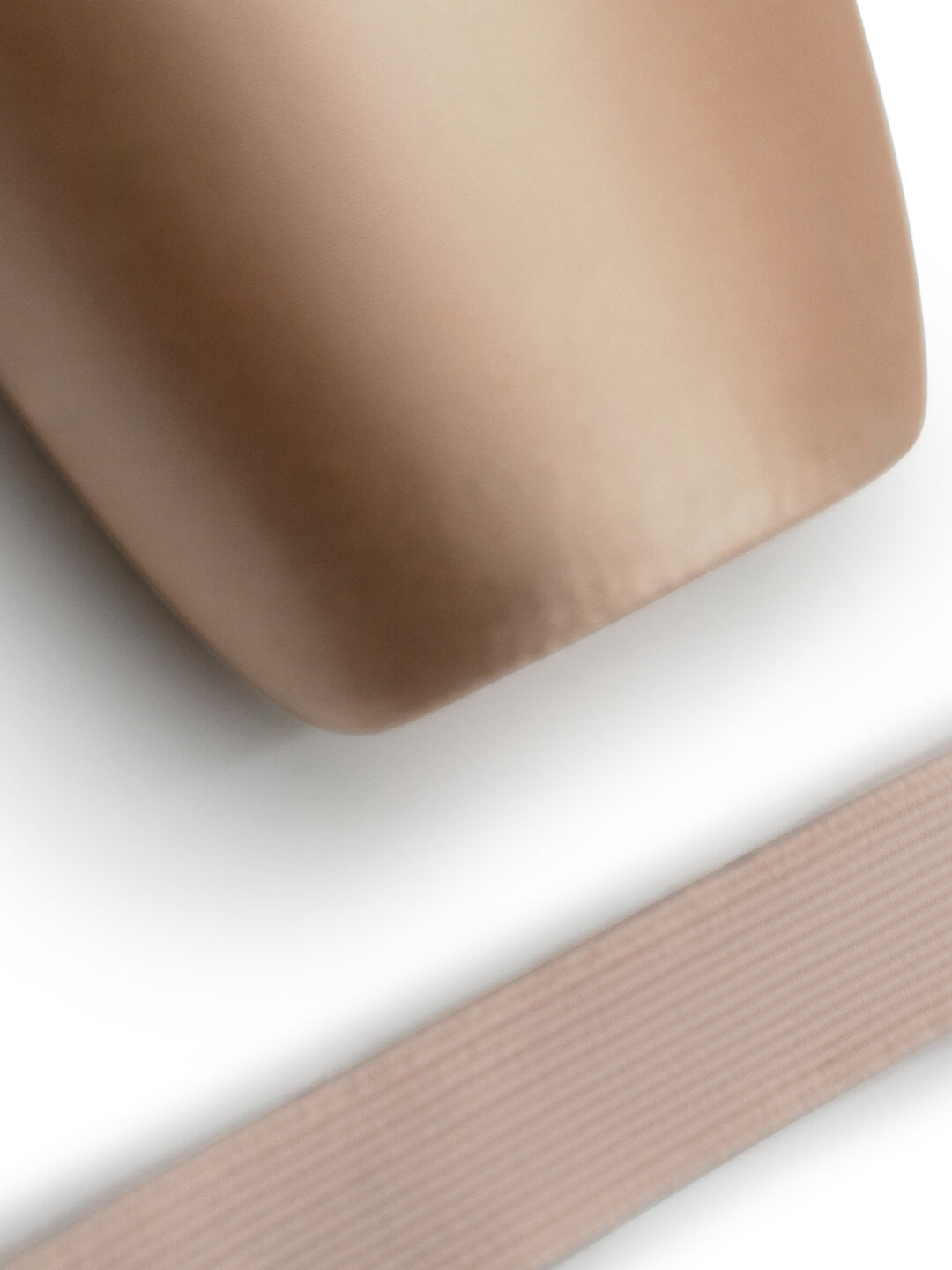 A close-up of a smooth, rounded beige object with a ribbed dusty pink strap or band running diagonally across the lower portion, set against a clean white background.
