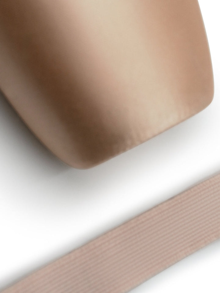 A close-up of a smooth, rounded beige object with a ribbed dusty pink strap or band running diagonally across the lower portion, set against a clean white background.