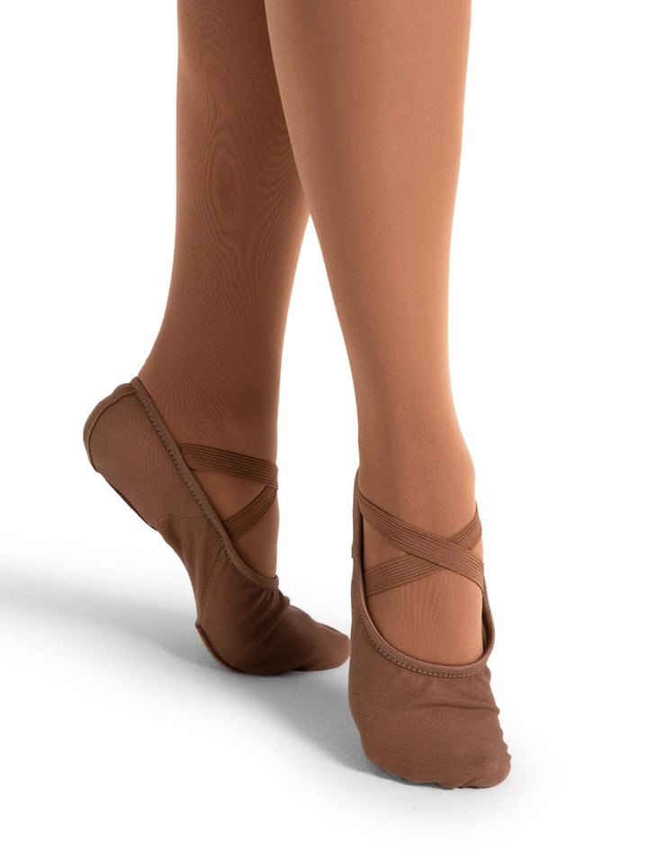 Brown ballet shoes worn with tights on a white background