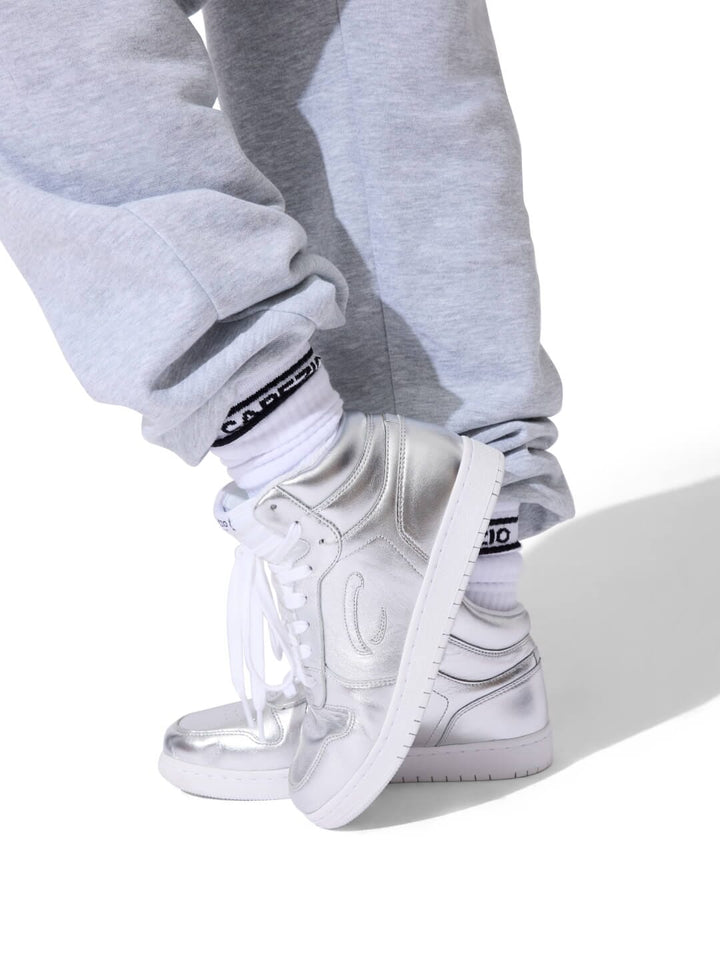 White sneakers with black accents worn with gray sweatpants on a white background